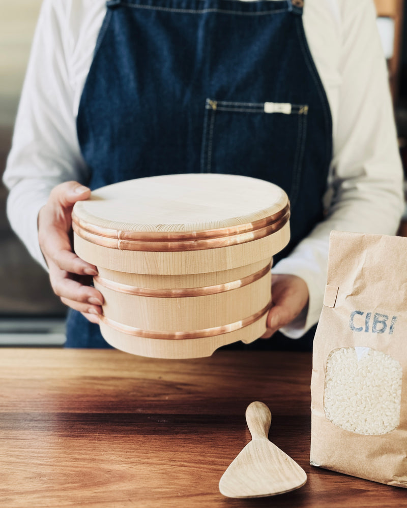 Yamacoh Cooked Rice Box "Ohitsu" 18cm (3.5cups) Person holding a rice box with a bag of rice on a wooden surface.